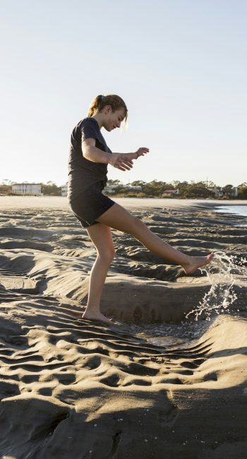 A teenage girl playing in sand dunes, at the beach